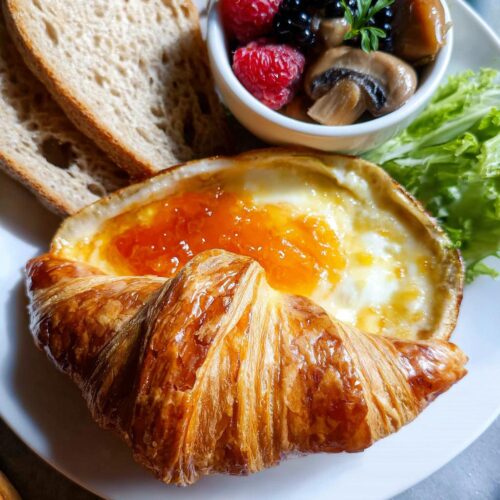 A baked croissant topped with melted cheese and apricot jam, served as part of a French Café Style Breakfast at Home.