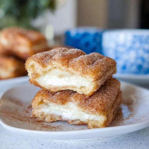 Two stacked Churro Cheesecake Bites cut in half, showing the creamy white filling inside the cinnamon-sugar coating.