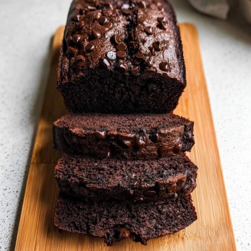 A loaf of rich, dark Double Chocolate Banana Bread, partially sliced, topped with melted chocolate chips.