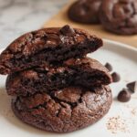 A stack of two fudgy Double Chocolate Cookies, with the top one broken open to show the gooey, melted chocolate chips inside.