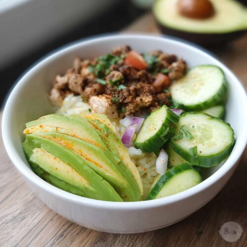 A white bowl containing an Easy Keto Lunch Idea with seasoned ground meat, sliced avocado, cucumbers, and red onion.