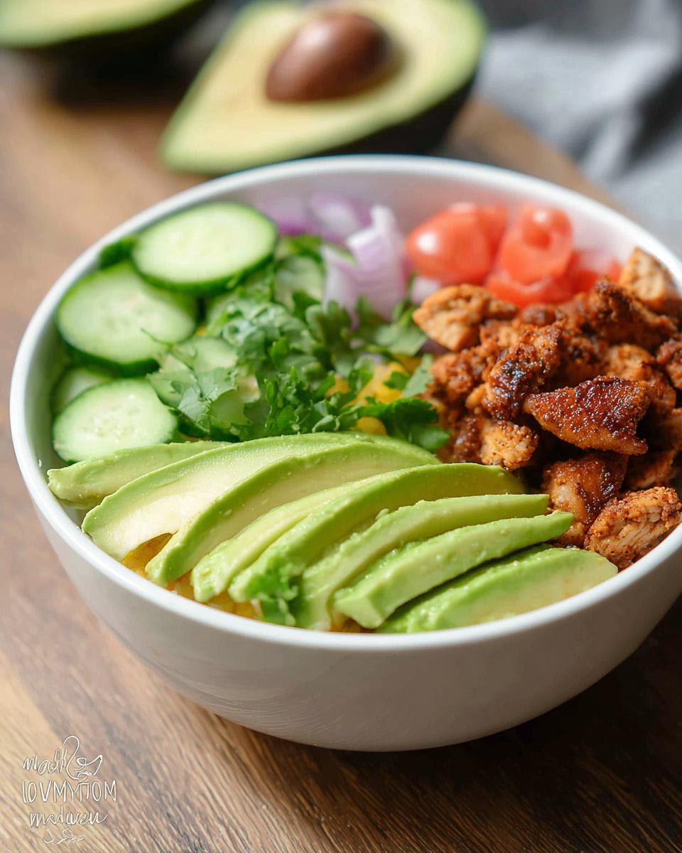 Close-up of a vibrant bowl featuring seasoned chicken, sliced avocado, cucumbers, and tomatoes, perfect for an Easy Keto Lunch Idea.