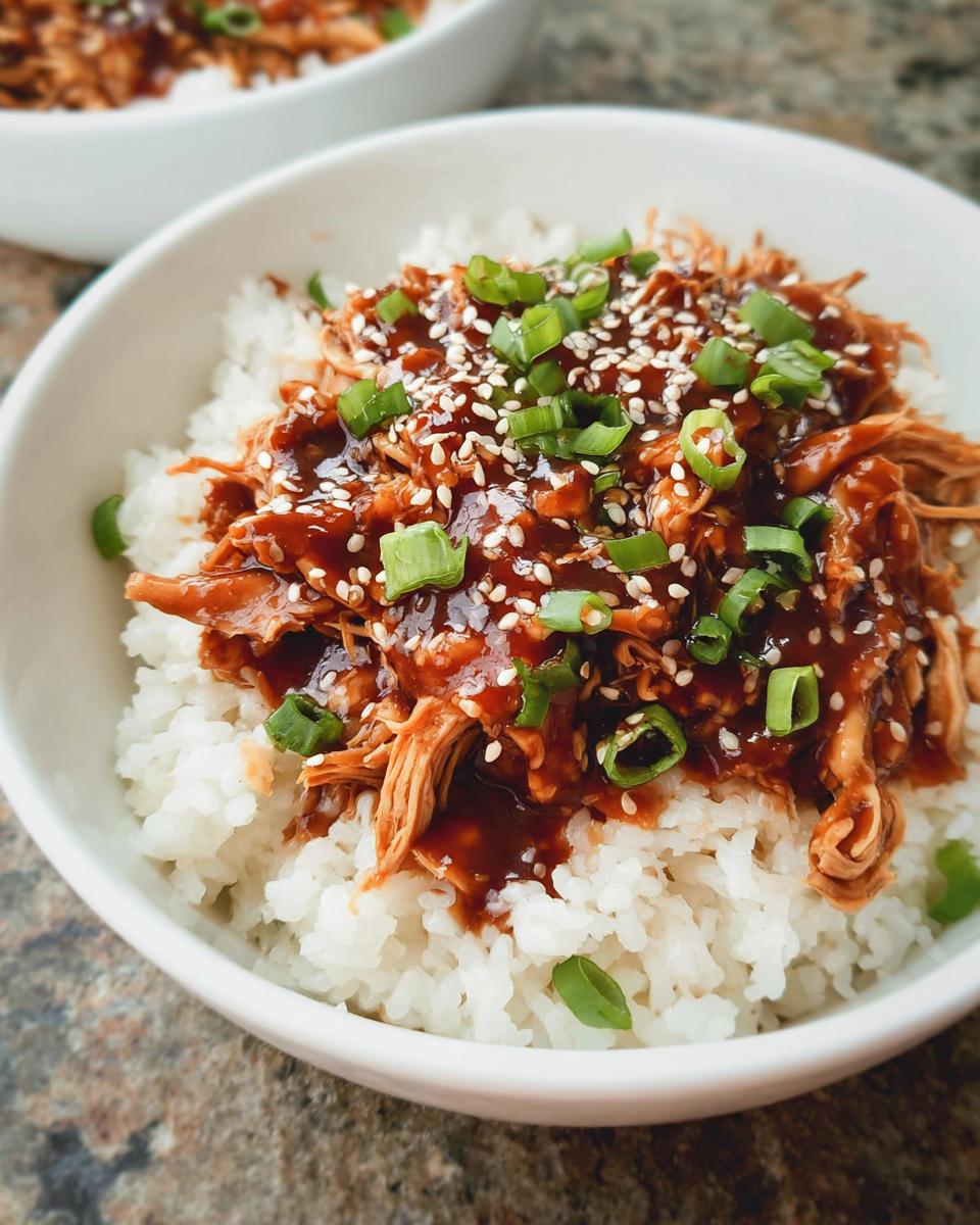 Close-up of shredded Family-Friendly Crockpot Teriyaki Chicken served over white rice, topped with sesame seeds and green onions.