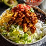 Close-up of a vibrant Chicken Taco Bowl featuring seasoned chicken, rice, black beans, lettuce, and shredded cheese.