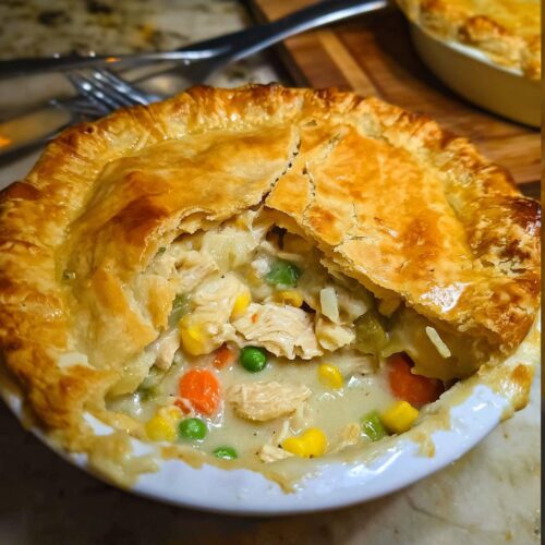 Close-up of a single-serving Freezer-Friendly Chicken Pot Pie with a golden, flaky crust broken open to show creamy filling and vegetables.