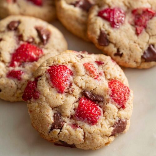 Close-up of several soft, baked Fresh Strawberry Cookies studded with bright red strawberry pieces and dark chocolate chunks.