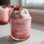 Close-up of a glass filled with light pink Fresh Strawberry Mousse, topped with whipped cream and a strawberry slice.
