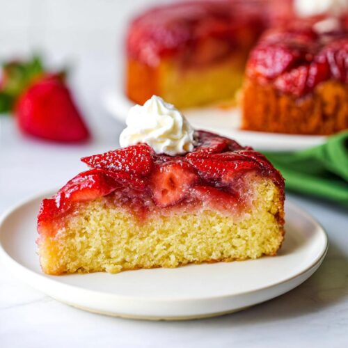 A moist slice of Fresh Strawberry Upside Down Cake topped with glazed strawberries and a dollop of whipped cream.
