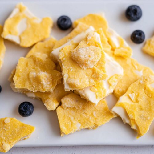 Close-up of broken pieces of bright yellow and white Frozen Lemon Yogurt Bark garnished with fresh blueberries.