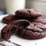 Close-up of fudgy Cocoa Powder Cookies, one broken in half showing the soft interior, sprinkled with sea salt.