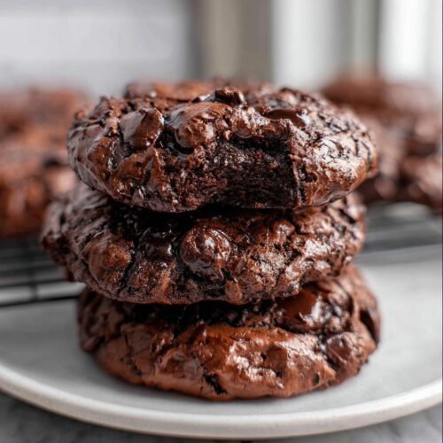 A stack of three intensely fudgy Flourless Chocolate Cookies, rich brown with melted chocolate chips.