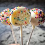 Close-up of three white chocolate coated Funfetti Cake Pops, one cut open to show the colorful cake interior.