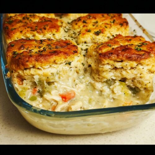 Close-up of creamy Garlic Herb Biscuit Chicken Pot Pie filling with visible carrots and celery under golden biscuits.