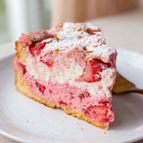 A close-up slice of Gooey Strawberry Cake featuring layers of pink strawberry filling and white cream, topped with powdered sugar.