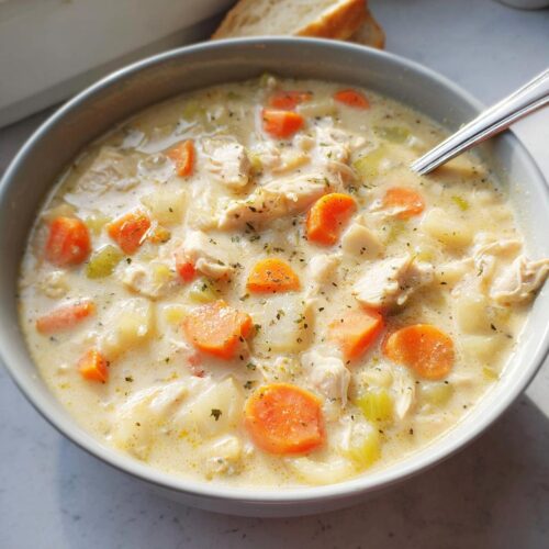 Close-up of a bowl of Healthy Creamy Chicken Soup filled with chunks of chicken, carrots, celery, and potatoes.
