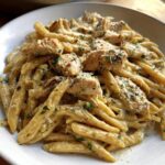 A bowl of Healthy Garlic Parmesan Chicken Pasta featuring penne coated in a creamy sauce with diced chicken and herbs.