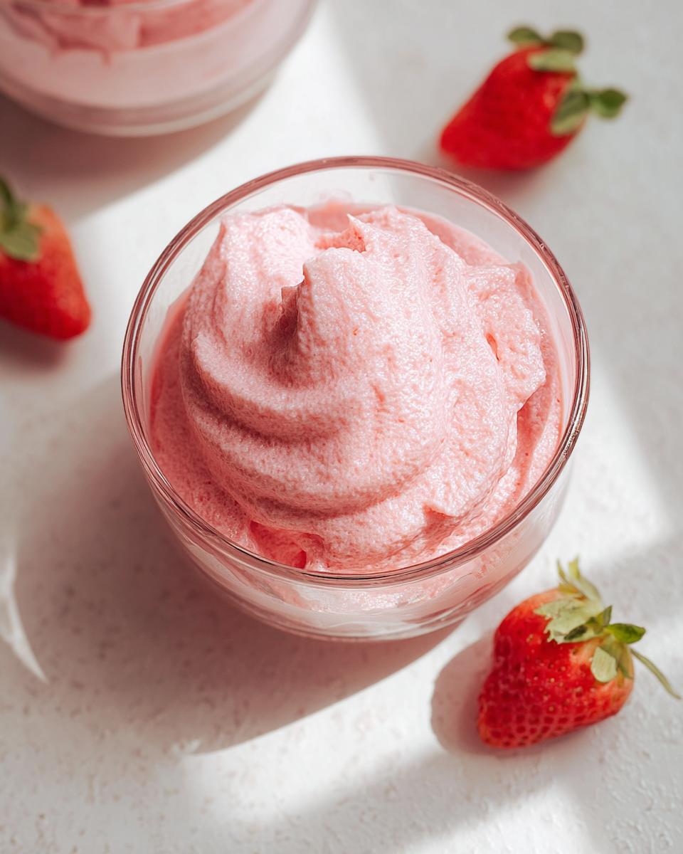 Close-up of fluffy pink Healthy Strawberry Mousse in a clear glass, garnished with fresh strawberries.