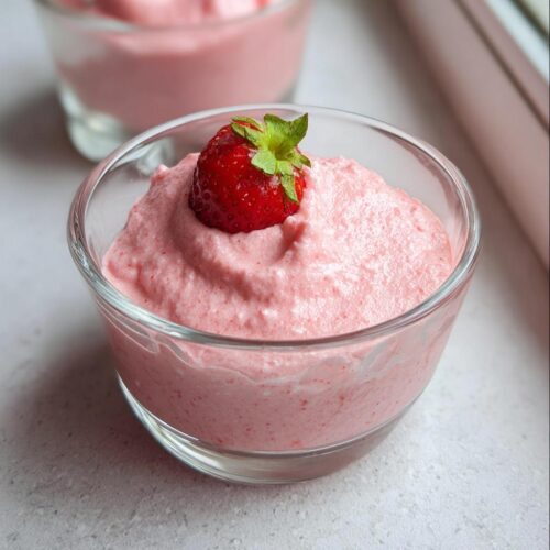 Close-up of a glass bowl filled with pink, fluffy Healthy Strawberry Mousse, topped with a whole fresh strawberry.