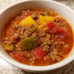 A close-up view of a white bowl filled with Hearty Stuffed Pepper Soup, featuring ground meat, tomatoes, and colorful bell pepper chunks.