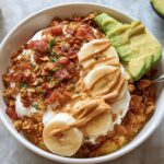 Overhead view of a High-Protein Breakfast Bowl topped with yogurt, bacon, banana slices, and peanut butter.