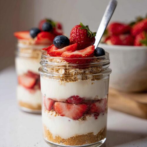Close-up of a layered High-Protein Cheesecake Jar with graham cracker crust, creamy filling, strawberries, and blueberries.