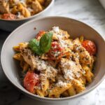 Close-up of a bowl of High Protein Chicken Pasta featuring penne, sliced chicken breast, roasted cherry tomatoes, and grated Parmesan.