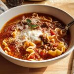 Close-up of a white bowl filled with rich, tomato-based High Protein Lasagna Soup, topped with ground meat, ricotta, and Parmesan.