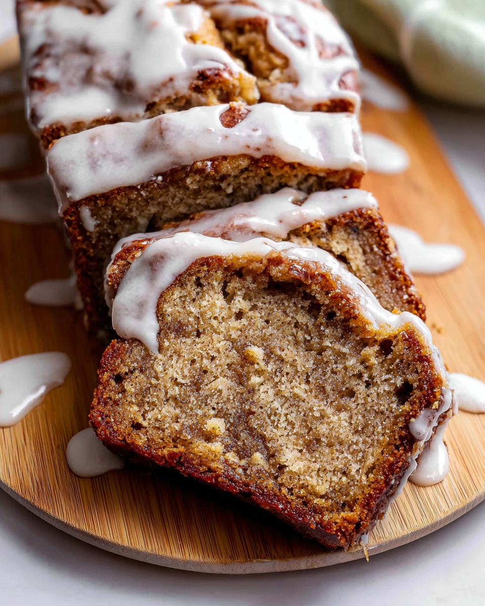Close-up of a sliced Iced Cinnamon Banana Loaf drizzled generously with white vanilla glaze on a wooden board.