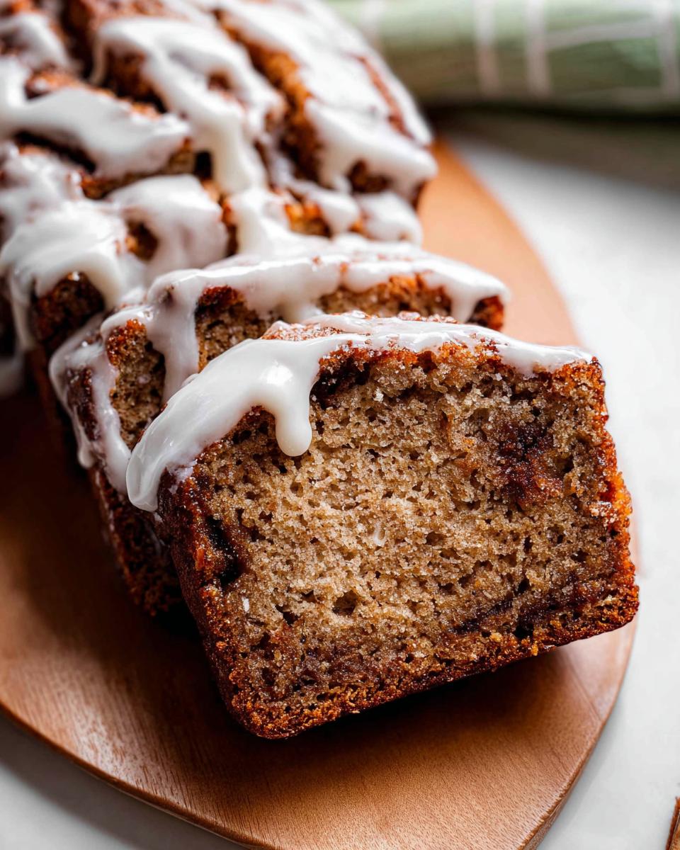 Close-up of sliced Iced Cinnamon Banana Loaf drizzled heavily with white glaze on a wooden board.