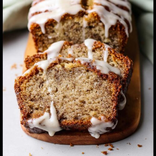 Two thick slices of moist Iced Cinnamon Banana Loaf drizzled with white glaze on a wooden board.