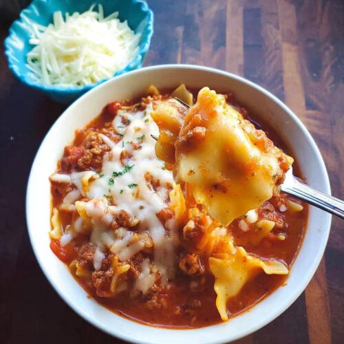 A fork lifts a piece of pasta from a bowl of rich Italian Sausage Lasagna Soup topped with melted mozzarella.