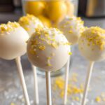 Close-up of several white chocolate covered Lemon Cake Pops topped with bright yellow lemon zest.