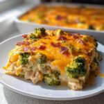 A slice of creamy Low Carb Chicken Casserole topped with melted cheddar cheese, broccoli florets, and bacon bits.