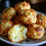 A pile of golden-brown Mashed Potato Jalapeño Cheese Puffs garnished with chives on a white plate.