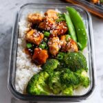 A glass container filled with Meal Prep Teriyaki Chicken Bowls featuring rice, glazed chicken, broccoli, and snap peas.