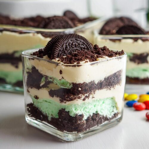 Close-up of an individual serving of Mint Oreo Dirt Cake layered with chocolate crumbs and mint cream in a square glass.