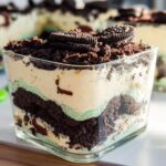 Close-up of an individual serving of Mint Oreo Dirt Cake layered with cream, mint filling, and crushed cookies.