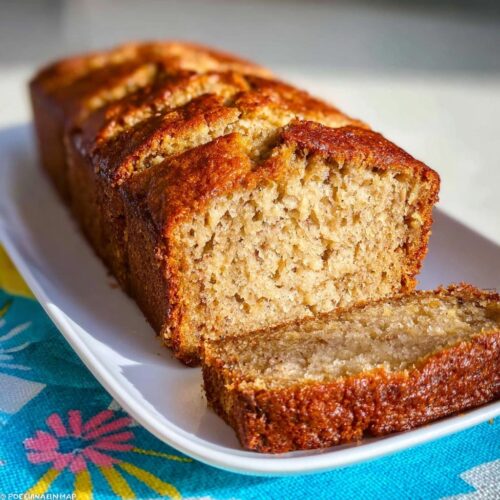 A golden-brown loaf of incredibly moist Sour Cream Banana Bread, with one slice cut and resting beside it.