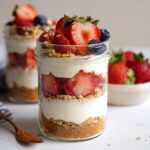 Close-up of a layered High-Protein Cheesecake Jar dessert topped with fresh strawberries and blueberries.