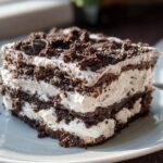 A close-up slice of No-Bake Oreo Icebox Cake showing layers of whipped cream and crushed chocolate cookies.