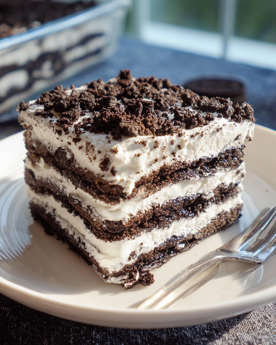 A perfect square slice of No-Bake Oreo Icebox Cake showing layers of cream and chocolate wafers, topped with crumbs.