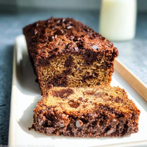 A close-up of moist No-Egg Chocolate Chip Banana Bread with one slice cut, showing rich chocolate chips throughout.