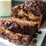 Two thick slices of rich No-Egg Chocolate Chip Banana Bread with melted chocolate chips, served next to the loaf.