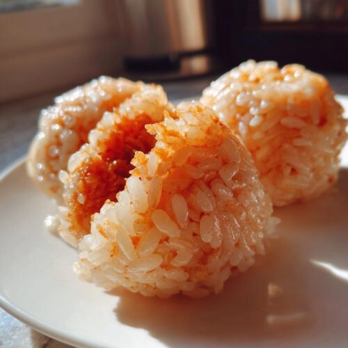 Three homemade No-Roll Sushi Balls made of sticky rice, one broken open to show the filling, served on a white plate.