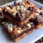 Close-up of stacked Nutella Magic Bars showing gooey chocolate layer, coconut, and chocolate chips on top.