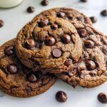 Three rich, dark brown One-Bowl Chocolate Cookies stacked slightly, studded with chocolate chips, on a white marble surface.
