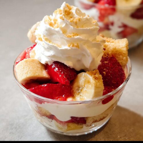 Close-up of a single serving of Party Strawberry Banana Dessert topped with whipped cream and crumbs.