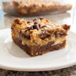 A rich, layered square of Peanut Butter Magic Bars topped with peanut butter swirls and chocolate chips on a white plate.