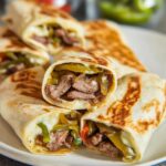 Close-up of several grilled Philly Cheesesteak Wrap Bites filled with steak, peppers, and melted cheese.