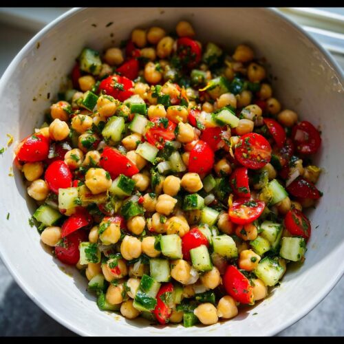 Close-up of a vibrant Quick Chickpea Salad featuring chickpeas, diced cucumbers, and halved cherry tomatoes in a white bowl.